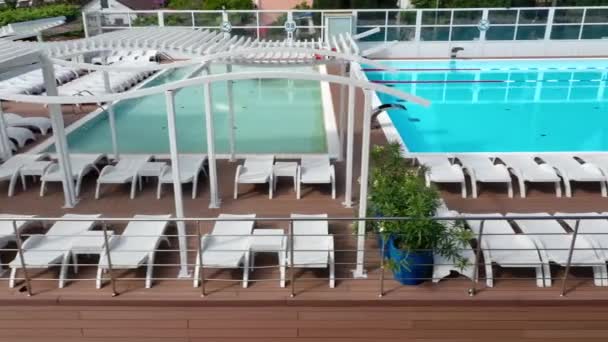 Εξωτερική πισίνα με κυματιστά γαλαζοπράσινα νερά και χαλύβδινα κάγκελα σκάλες. Σκάλα από ανοξείδωτο χερούλια για κάθοδο στην πισίνα. Αεροφωτογραφία της δημόσιας πισίνας — Αρχείο Βίντεο