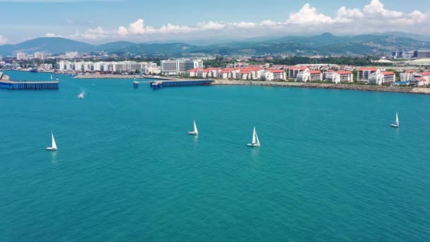 Aerial shot of sailing yachts at the race-regatta on the sea, cityscape on the background. Ranks from yachts of participants of a regatta goes on a start point, is a sailing race at Sochi. — Stock Video