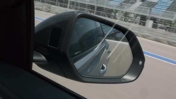 Черный автомобиль в движении, дорога отражена в боковом зеркале, междугороднее зеркало автомобиля. Другой автомобиль следует за ним на заднем сиденье движущейся машины. от зеркала бокового вида. — стоковое видео