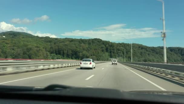 夏の晴れた日に道路の車の窓から青空を表示します。自然。車の風景に沿って運転。旅行、旅行、車での旅。輸送コンセプト。高速道路だ。車の忙しい交通。近代的な道路. — ストック動画