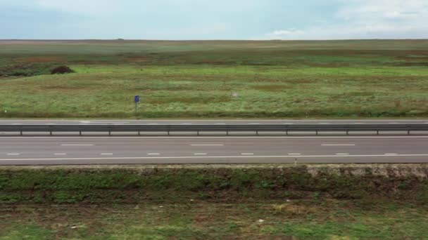 Bilar kör på en modern flerfilig motorväg mot bakgrund av ett grönt fält. Kamerans parallella rörelse. Flygfilminspelning. En solig dag. Transporter. — Stockvideo