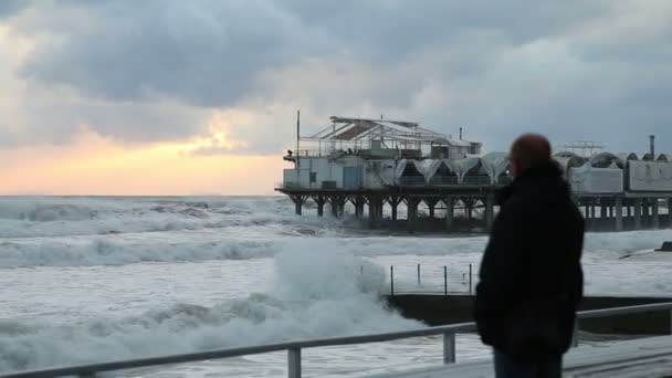O homem em mau tempo está na costa e olha para a tempestade. No fundo de um restaurante à beira-mar. Sochi. — Vídeo de Stock