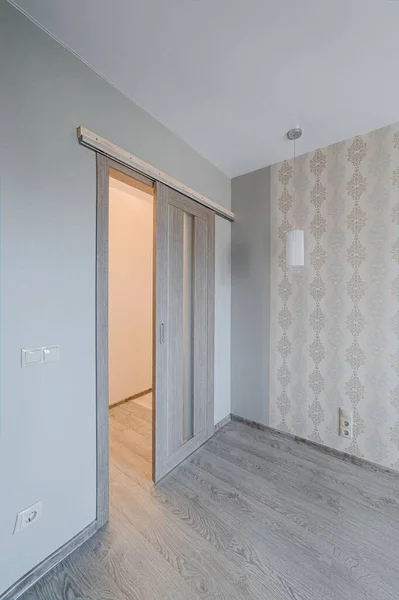 Sliding door in finishing apartment interior. Empty room in new building with repair, walls with wallpapers. Repair works on construction site of residential apartment.