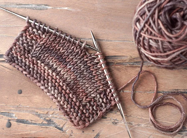 Wool yarn and knitting needles laying on the wooden background.