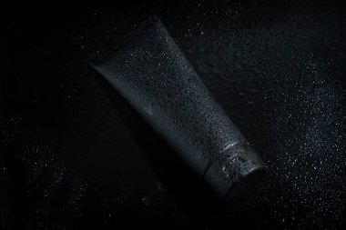 Güzellik modası makyaj malzemelerinin maketi. Su damlası arka planında cilt sağlığı konsepti olan siyah şişe losyonu.