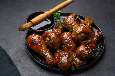 glazed teriyaki chicken legs on black plate, selective focus clipart