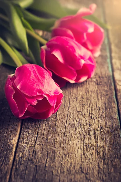 Tři růžové tulipány na dřevěný stůl, tónovaný — Stock fotografie
