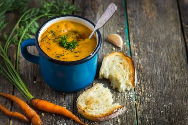 carrot  soup in blue mug on rustic background clipart