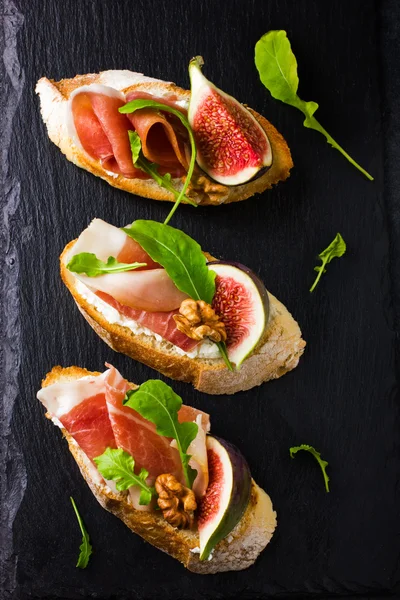 Bruschetta with goat cheese, figs, prosciutto and arugula — Stock Photo, Image