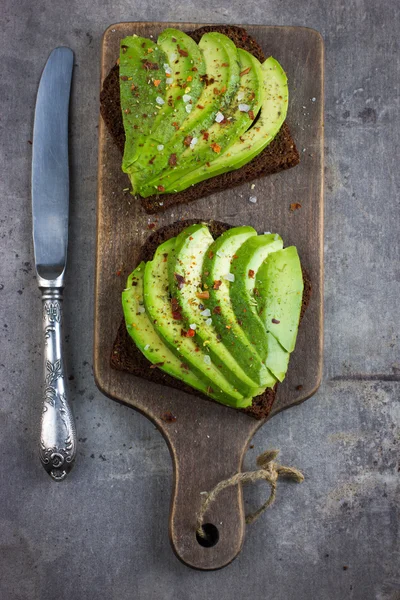 Rye toasts with avocado on wooden cutting board — Stock Photo, Image