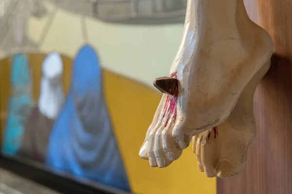 Nailed feet, detail of wooden statue of Jesus Christ crucified in a defocused background.
