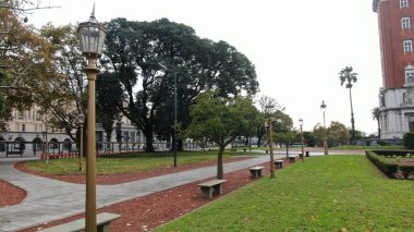 Buenos Aires, Arjantin 'in Buenos Aires şehir merkezindeki boş bir caddenin geniş açıyla görüntüsü. Sahnede, dükkanlar ve konut birimleri de dahil olmak üzere caddenin her iki tarafını kaplayan yüksek binalar yer alıyor. Belirgin işaretler