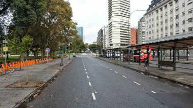 Buenos Aires, Arjantin 'in Buenos Aires şehir merkezindeki boş bir caddenin geniş açıyla görüntüsü. Sahnede, dükkanlar ve konut birimleri de dahil olmak üzere caddenin her iki tarafını kaplayan yüksek binalar yer alıyor. Belirgin işaretler