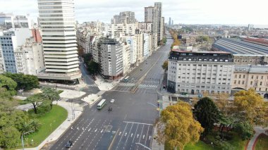 Buenos Aires, Arjantin 'in Buenos Aires şehir merkezindeki boş bir caddenin geniş açıyla görüntüsü. Sahnede, dükkanlar ve konut birimleri de dahil olmak üzere caddenin her iki tarafını kaplayan yüksek binalar yer alıyor. Belirgin işaretler