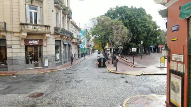 Buenos Aires, Arjantin 'in Buenos Aires şehir merkezindeki boş bir caddenin geniş açıyla görüntüsü. Sahnede, dükkanlar ve konut birimleri de dahil olmak üzere caddenin her iki tarafını kaplayan yüksek binalar yer alıyor. Belirgin işaretler