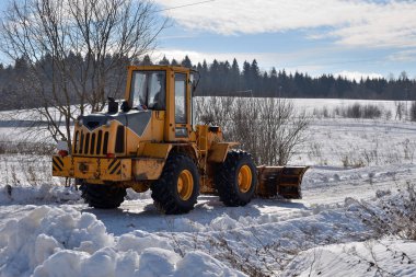Traktör, kış güneşli bir günde köyün yolunu temizler.