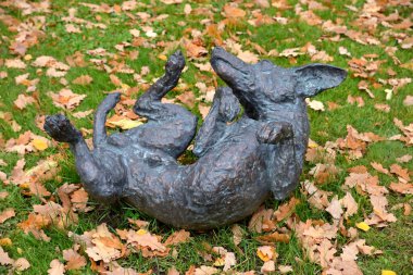Moskova, Rusya, 14 Ekim 2019: Moskova Devlet Üniversitesi Botanik Bahçesi 'ndeki sarı meşe yapraklarıyla çimenlikte hoplayıp zıplayan köpek heykeli