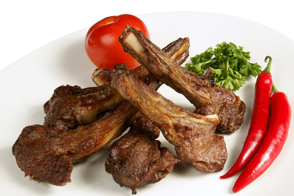 Grilled meat on the bone with fresh vegetables on white plate