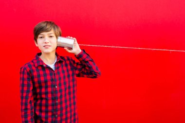 Çocuk kırmızı duvara karşı iki metal kutu ve bir ip kullanıyor.
