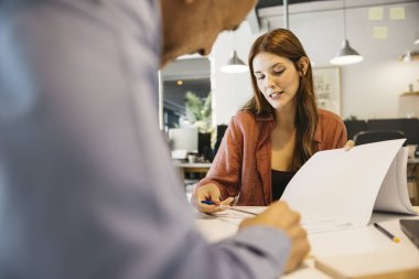 Genç kadın ve adam belgeleri inceliyor ve bir projede işbirliği yapıyorlar.