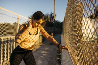 Atletik kadın çite yaslanıyor, altın saatinde spor ve spor yapıyor.
