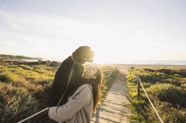 Siyah Labrador 'u kucaklayan bir kadın, altın saatinde sahile giden bir yolda.