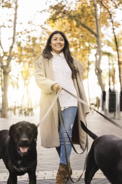 Gülümseyen kadın, güz boyunca şehir parkında tasmalı iki evcil köpekle geziyor.