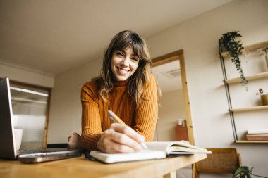 Genç bir kadın iş yerindeki bir planlamacıya notlar yazarken gülümsüyor.