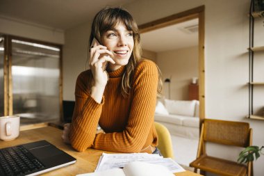 Gülümseyen bir kadın ev telefonuyla konuşuyor.