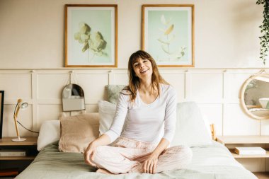 Evde yatağında oturmuş gülümseyen genç bir kadın.