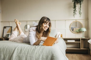 Yatak odasında kitap okurken gülümseyen bir kadın.