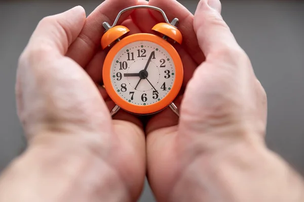 ヤシの中に小さなオレンジ色の目覚まし時計を持って白人男性の手 時間の概念 — ストック写真