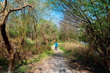 Collegno, İtalya. 5 Nisan 2021. Dora Riparia Parkı. Park yolu boyunca, bir bahar günü sırt çantalı bir kadın ağaçların arasında yürür..