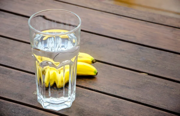 Vaso de agua y dos plátanos sobre fondo de madera — Foto de Stock