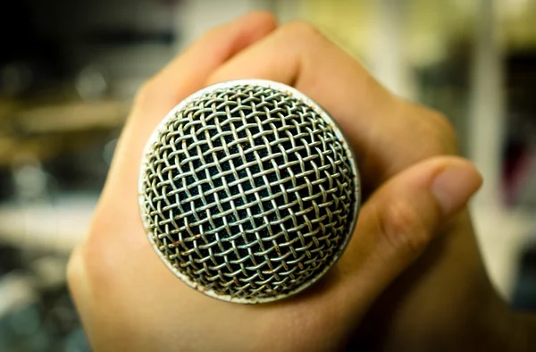 Manos sosteniendo un micrófono en la sala de música — Foto de Stock