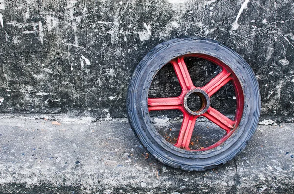 Vieja rueda roja apoyada en una vieja pared grunge — Foto de Stock