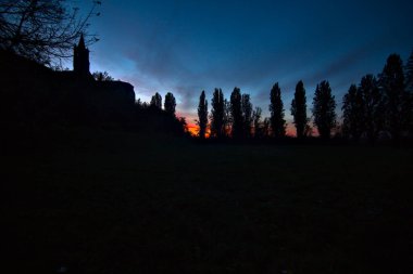 Sonbaharda günbatımında selvi ile çevrili bir kilisenin arkasındaki açık alan.