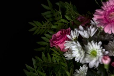Bir buket pembe karanfil ve beyaz kasımpatı ve siyah arka planda pembe gerberalar olan bir gül.