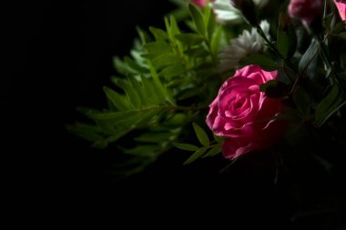 Bir buket pembe karanfil ve beyaz kasımpatı ve siyah arka planda pembe gerberalar olan bir gül.