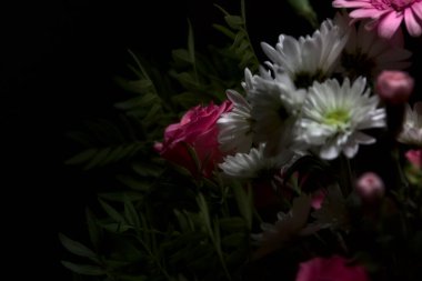 Bir buket pembe karanfil ve beyaz kasımpatı ve siyah arka planda pembe gerberalar olan bir gül.