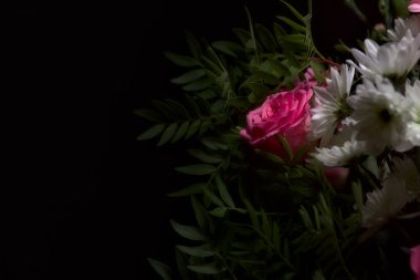 Bir buket pembe karanfil ve beyaz kasımpatı ve siyah arka planda pembe gerberalar olan bir gül.