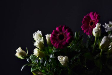 Beyaz güller, kasımpatılar, mor gerberalar ve siyah arka planda güller.