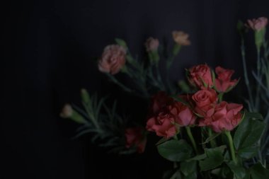 Siyah arka planda kırmızı küçük güller ve turuncu karanfiller.