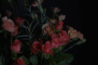 Siyah arka planda kırmızı küçük güller ve turuncu karanfiller.