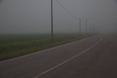 Sonbaharın sonlarında sisli bir günde İtalya kırsalında tarla ile çevrili bir yol.