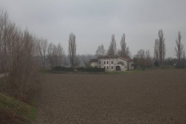 Sonbaharın sonlarında İtalya kırsalında çıplak ağaçlarla tarlalı bir tarlanın ortasında bir kır evi.