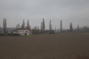 Sonbaharın sonlarında İtalya kırsalında çıplak ağaçlarla tarlalı bir tarlanın ortasında bir kır evi.