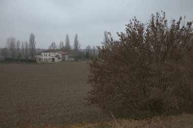 Sonbaharın sonlarında İtalya kırsalında çıplak ağaçlarla tarlalı bir tarlanın ortasında bir kır evi.