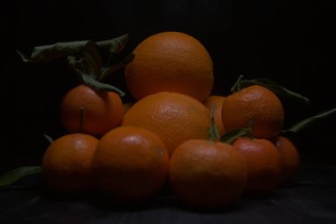 Portakallar ve mandalinalar siyah bir yüzeye dizilmiş.