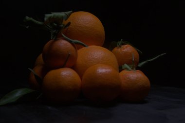 Portakallar ve mandalinalar siyah bir yüzeye dizilmiş.